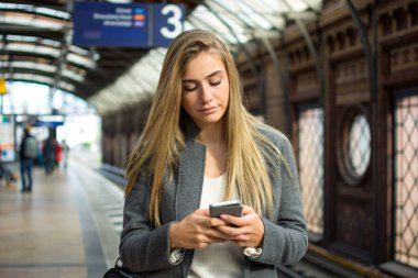 Tren istasyonunda telefon kullanan genç bir kadının portresi.