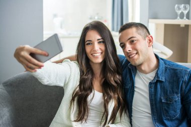 Genç çift evde akıllı telefonlarıyla selfie çekiyor.