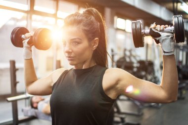 Güzel bir genç bayan spor salonunda dambıllarla çalışıyor.