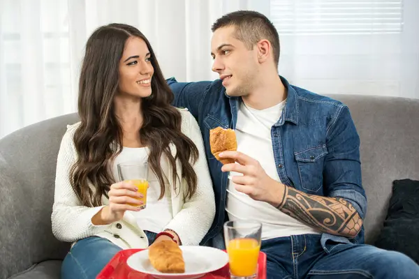 一对年轻夫妇坐在沙发上一起吃早餐 — 图库照片
