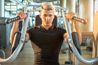 Spor salonunda kollarını esneten genç yakışıklı adam. Sarışın kaslı adam spor salonunda çalışıyor.