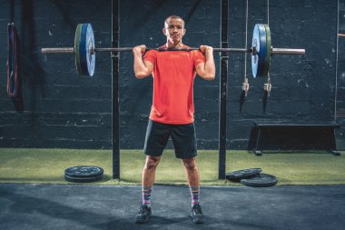 Spor giyimli formalı sporcu spor salonunda halter kaldırıyor.