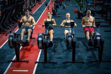 Spor salonundaki kürek makinelerinde çalışan bir grup sporcu.