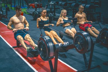 Spor salonundaki kürek makinelerinde çalışan bir grup sporcu.