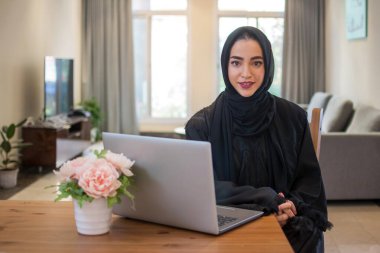 Genç Arap iş kadını evde dizüstü bilgisayarla başörtüsü giyiyor.