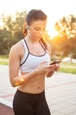 Genç bayan koşucu şehirde bir rıhtımda mola verip müzik dinliyor.