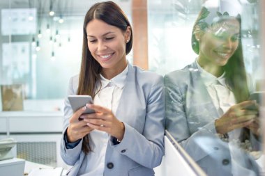 Modern ofiste cep telefonu kullanan genç bir iş kadını