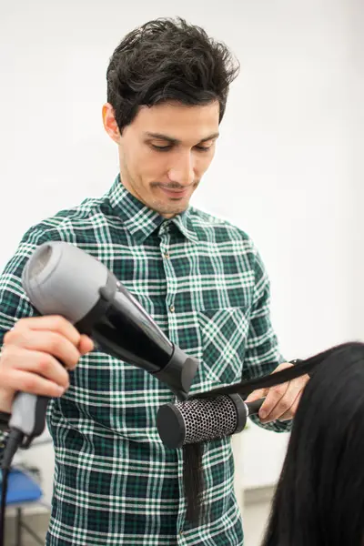 Hairdresser drying long black hair with hair dryer and round brush