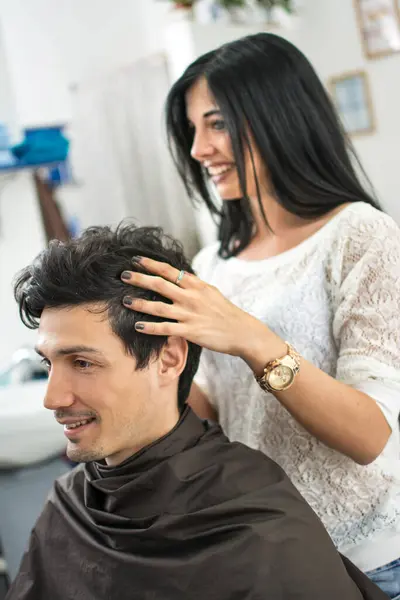 Female hairdresser making hairstyle for a male client at hair salon