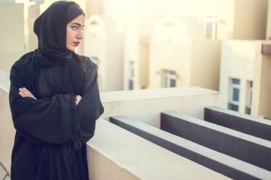 Ortadoğulu güzel bir kadının portresi çapraz kollarıyla balkonun manzarasının keyfini çıkarıyor.