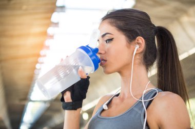 Koşu sırasında su içen sportif kız dışarıda mola veriyor.