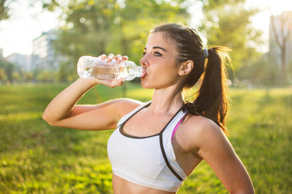 Young smiling woman drinking water from bottle after fitness sport exercise outdoors at sunset
