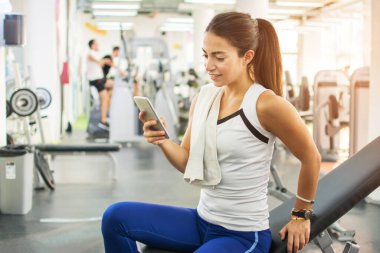 Spor salonunda akıllı telefon kullanan genç bir fitness kadını.