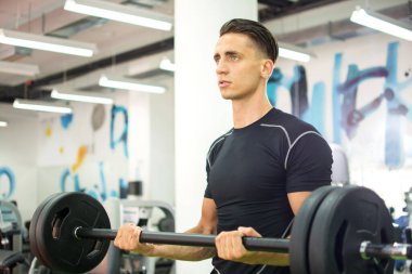 Genç yakışıklı adam spor salonunda halterle çalışıyor..