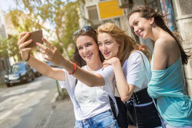 Gülümseyen genç kızlar dışarıda selfie çekiyorlar.