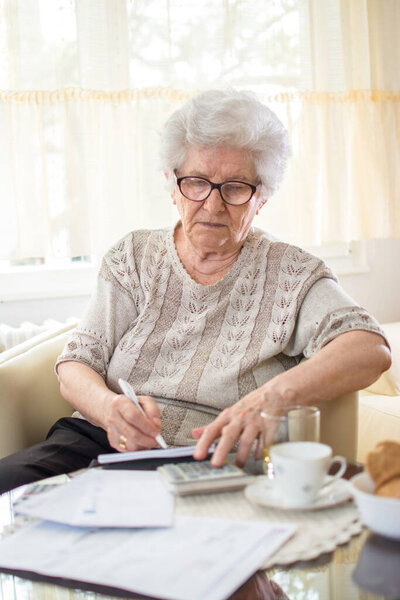 Senior woman calculating bills at home.