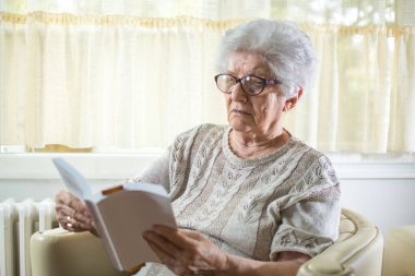 Evde kitap okuyan kıdemli bir kadın..