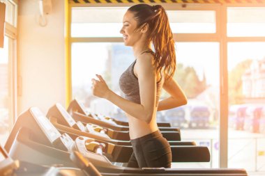 Spor salonunda koşu bandında koşan zayıf kızın yan görüntüsü..