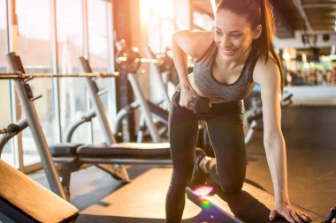 Neşeli sporcu kadın spor salonunda ağırlık kaldırıyor.