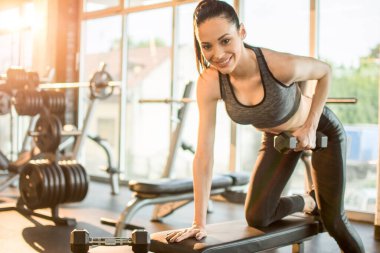 Spor giyimli zayıf genç bir kadın spor salonunda ağırlık çalışıyor..