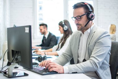 Çağrı merkezinde bilgisayar üzerinde çalışan konsantre erkek teknik destek operatörü