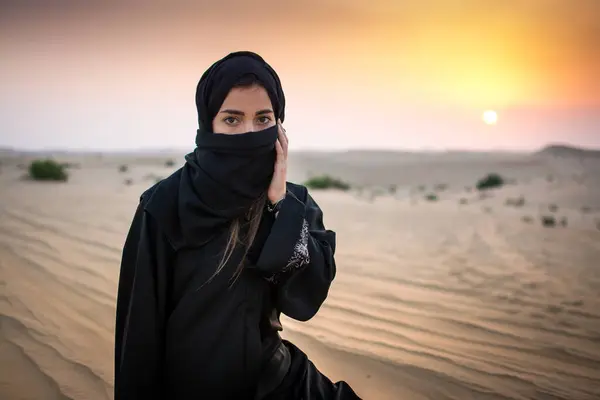 一个年轻的阿拉伯女人穿着传统的黑色衣服在美丽的落日下在沙漠中的画像 — 图库照片