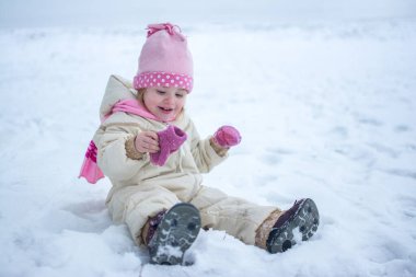Küçük kız karda oturuyor ve eğleniyor