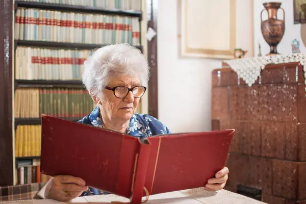 Starsza Kobieta Ogląda Album Fotograficzny Salonie Domu — Zdjęcie stockowe