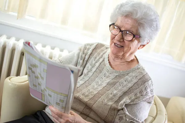 快乐的老年妇女在家里解决纵横字谜 — 图库照片