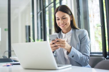 Beautiful young business woman using phone in office.