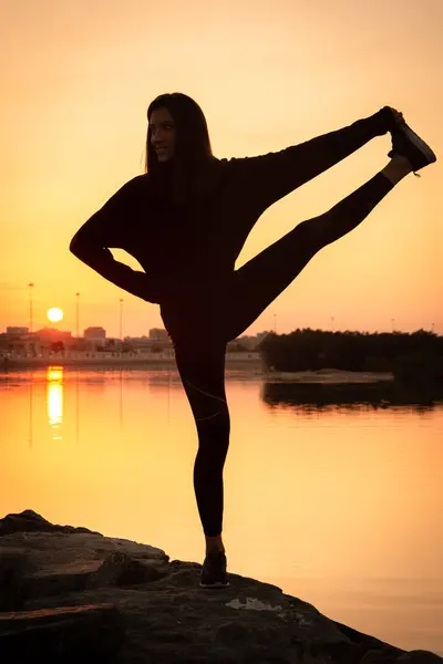 一个美丽的瑜伽女子在靠近海岸的日出或日落时进行平衡运动的轮廓 — 图库照片