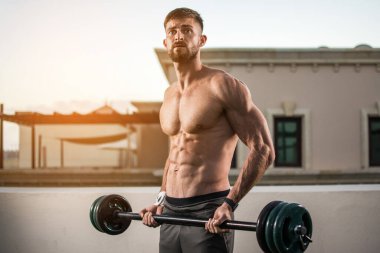 Kas sakallı adam dışarıda halterlerle egzersiz yapıyor..