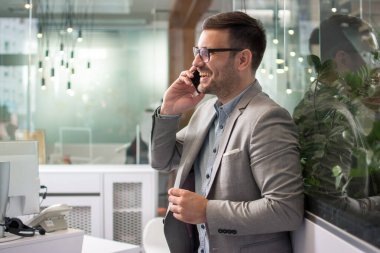 Resmi kıyafetli gülümseyen bir adamın cep telefonuyla konuşmasının yan görünümü..