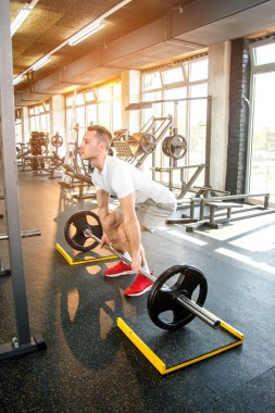Spor salonunda ağırlık kaldıran sağlıklı bir gencin tam boy portresi.