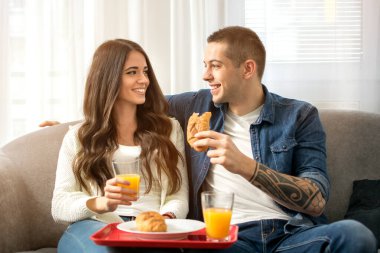 Genç çift evdeki kanepede dinlenirken birlikte kahvaltı yapıyor.