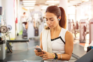 Spor salonunda kulaklığı ve akıllı telefonu olan sportif bir kız..