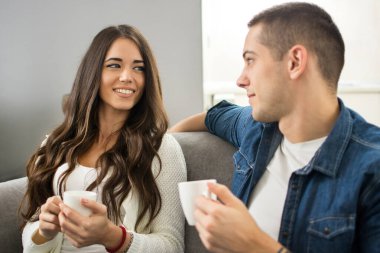 Kahve fincanları olan genç bir çift evde konuşuyor.