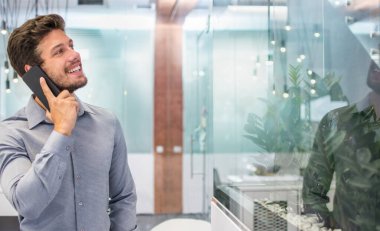 Modern ofiste cep telefonuyla konuşan yakışıklı genç adam..