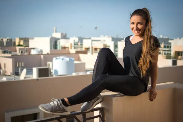 Spor Kıyafetli Gülümseyen Genç Bir Kadın Çatıda Oturuyor — Stok fotoğraf