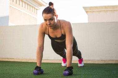 Damda dambıllarla şınav çeken sportif kız, açık havada spor salonu..