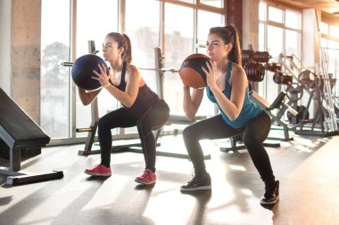 Çekici genç kadınlar spor salonunda pilates topuyla egzersiz yapıyorlar..