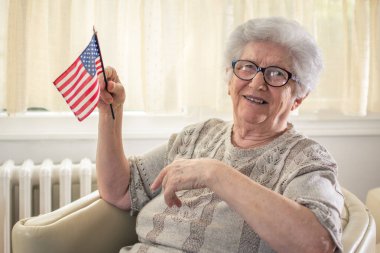 Amerikan bayrağıyla evdeki rahat koltukta oturan yaşlı kadın..