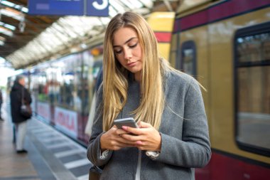 Tren istasyonunda telefon kullanan genç bir kadının portresi..