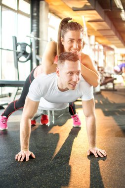 Spor salonunda birlikte egzersiz yapan genç bir çift. Kız üzerine yatarken adam şınav çekiyor.