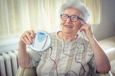 Cheerful senior woman listening to music on CD player at home. clipart