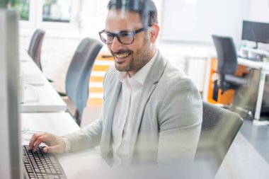 Ofiste bilgisayar kullanan neşeli bir işadamı.