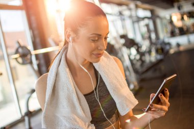 Spor salonunda akıllı telefon kullanan kulaklıklı genç bayan portresi..