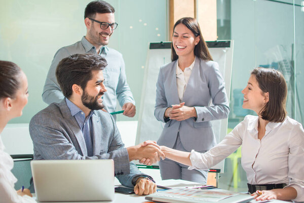 Group of business people welcoming young female colleague to their team. Friendly business people shaking hands with colleagues around them in the office.