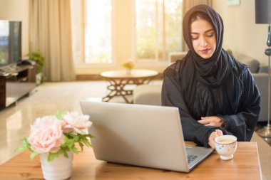 genç Müslüman kadın kahve içme ve dizüstü evde kullanma.