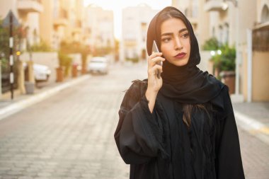 Şehir caddesinde tesettürlü güzel bir Arap iş kadını cep telefonuyla konuşurken portresi.